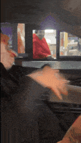 a woman in a red shirt is standing behind a drive through window