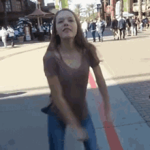 a woman in a brown shirt and blue jeans is dancing on the sidewalk