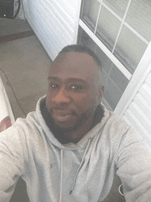 a man wearing a grey hoodie is taking a selfie in front of a white building
