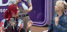 a man with red hair is talking into a microphone while another man holds a card that says idol