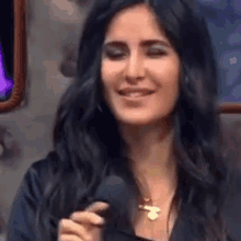 a woman with long black hair is holding a microphone and smiling while wearing a necklace .