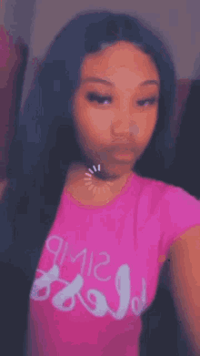 a girl with long black hair is wearing a pink shirt and a choker .