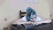 a girl with blue hair is sitting at a desk with a laptop