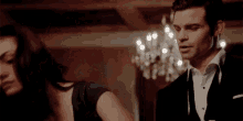 a man in a tuxedo and tie is standing next to a woman in a room .