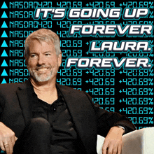 a man sitting in front of a screen that says it 's going up forever laura forever
