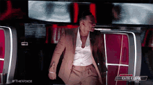 a man in a tan suit is standing in front of a screen that says #thevoice on it