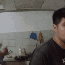 a man in a black shirt with the letter n on it is standing in a kitchen