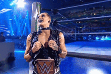 a woman is standing in a wrestling ring holding a wrestling championship belt .