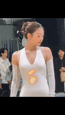a woman wearing a white dress with a flame on her chest
