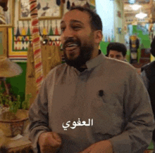 a man with a beard is laughing in a room with arabic writing on his shirt .