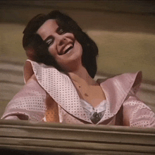 a woman in a pink dress is laughing and looking out of a window
