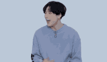 a man in a blue sweater is laughing with his mouth open and his hands on his chest .