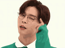 a young man wearing glasses and a green sweater is making a face .