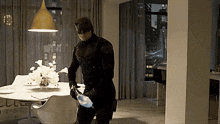 a man in a daredevil costume is standing in a dining room next to a table and chairs .