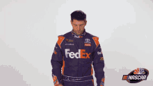 a man in a fedex racing suit is standing with his arms crossed .
