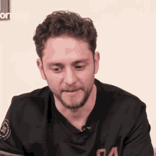a man with curly hair and a beard is wearing a black jersey with the letter a on it