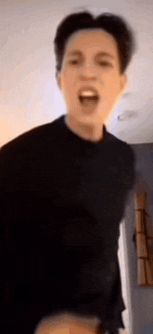 a man in a black shirt is standing in a room with his mouth open and making a funny face .