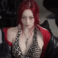 a woman with red hair and a leopard print top is wearing a red jacket and a necklace .