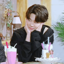 a young man is sitting at a table with a pink milkshake and straws