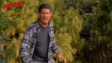 a man in a plaid shirt is standing in front of trees and the word baywatch is on the bottom