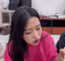 a woman in a pink shirt is sitting on a couch and making a funny face .