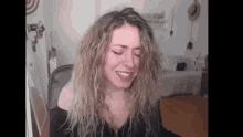 a woman with curly hair is smiling and making a funny face while sitting in a chair .