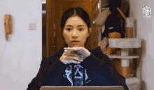a woman wearing a black hoodie with a cat on it looks at a laptop
