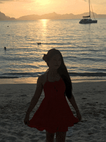 a woman in a red dress is standing on the beach at sunset