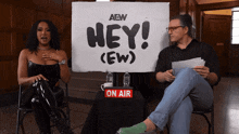 a man and a woman sit in front of a sign that says hey ( ew )