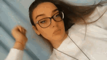 a young woman wearing glasses and a white sweater is laying down on a bed .