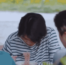 a woman in a striped shirt is eating noodles with chopsticks while sitting at a table .