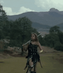 a woman is holding a sword in a field with mountains in the background