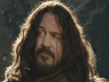 a man with long hair and a beard looks to his left
