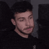 a man with a beard is wearing a black shirt with a white x on it