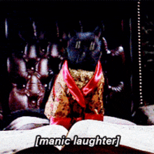 a black cat in a devil costume sits on a book with the words " manic laughter " written below it