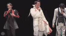 a man in a white coat is singing into a microphone while two other men look on