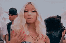 a woman with blonde hair and red nails is standing in front of a group of people .