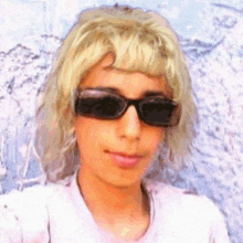 a woman wearing sunglasses and a wig looks at the camera