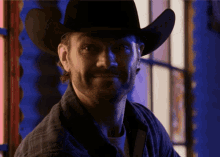 a man wearing a cowboy hat and plaid shirt smiles