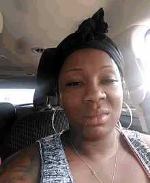 a woman wearing a black turban and hoop earrings looks at the camera