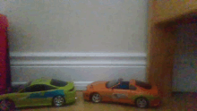 a green toy car and an orange toy car are sitting on a wooden floor