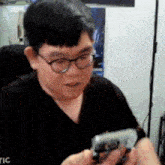 a man wearing glasses and a black shirt is holding a cell phone .