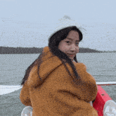 a girl wearing a white hat and a brown jacket is sitting on a boat