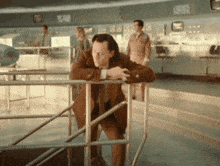 a man in a suit leaning on a railing in a control room .