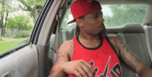 a man is sitting in the back seat of a car wearing a red hat and a red tank top .