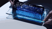 a person is holding a blue block of ice on a glass tray