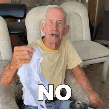 an elderly man is sitting in a chair holding a white cloth with the word no written on it