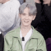 a young man with gray hair is wearing a green jacket and a white shirt .