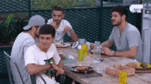 a group of men are sitting at a table eating food and drinking water .