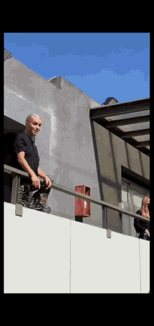 a man in a black shirt is standing on a balcony with a red box in front of him